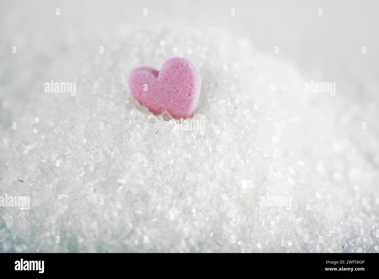 Weißer Kristallzucker mit Herzbonbons auf weißem Hintergrund Stockfoto