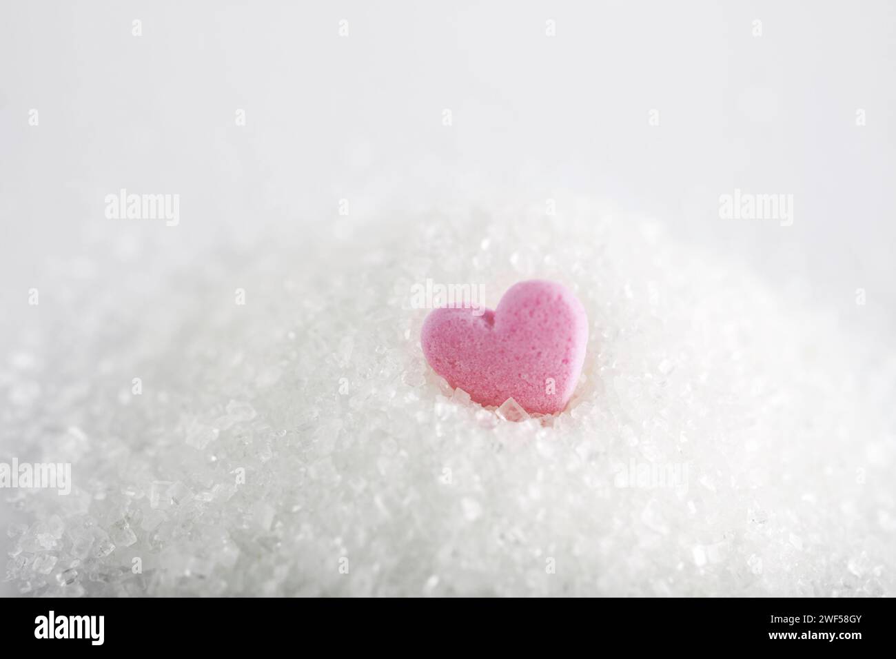 Weißer Kristallzucker mit Herzbonbons auf weißem Hintergrund Stockfoto