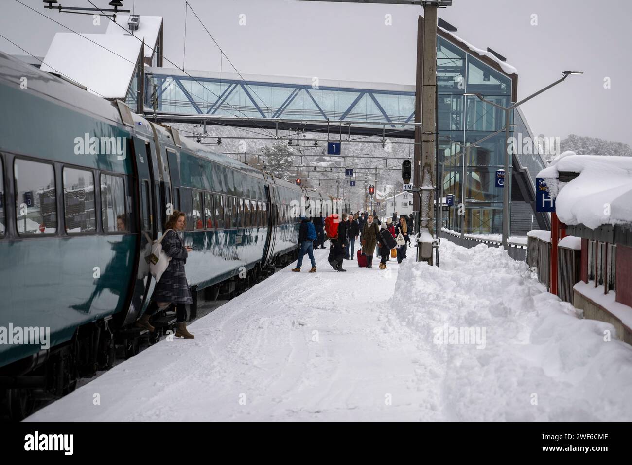 Geilo, Viken, Norwegen. November 2023. Mehrere Passagiere werden beim Aussteigen aus dem Zug und beim Spaziergang entlang des Bahnsteigs Gelio gesehen. Die Bergensbanen-Zugstrecke ist ein Eisenbahnerlebnis, das Reisenden eine malerische Reise durch Norwegens atemberaubendste Landschaften bietet. Die Bahnstrecke bietet eine Verbindung in die nordische Wildnis, da der Zug über Hochplateaus, Fjorde, Flüsse und atemberaubende Panoramen führt. Die Züge bieten Annehmlichkeiten an Bord, darunter Restaurantwagen, in denen Passagiere norwegische Speisen und Getränke genießen können, während sie die Landschaft vorbeiziehen sehen. (Cred Stockfoto