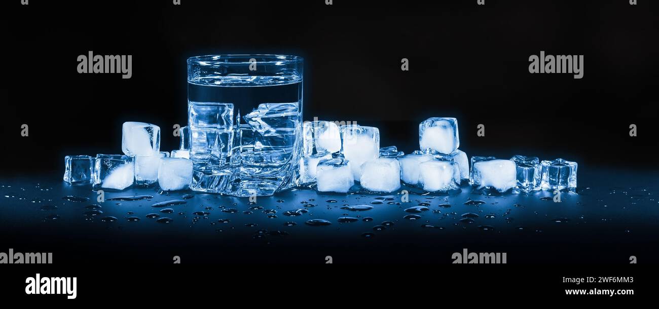 Gekühltes sauberes Wasser in einem Glas vor einem Hintergrund aus Eiswürfeln, auf dunklem Hintergrund Stockfoto