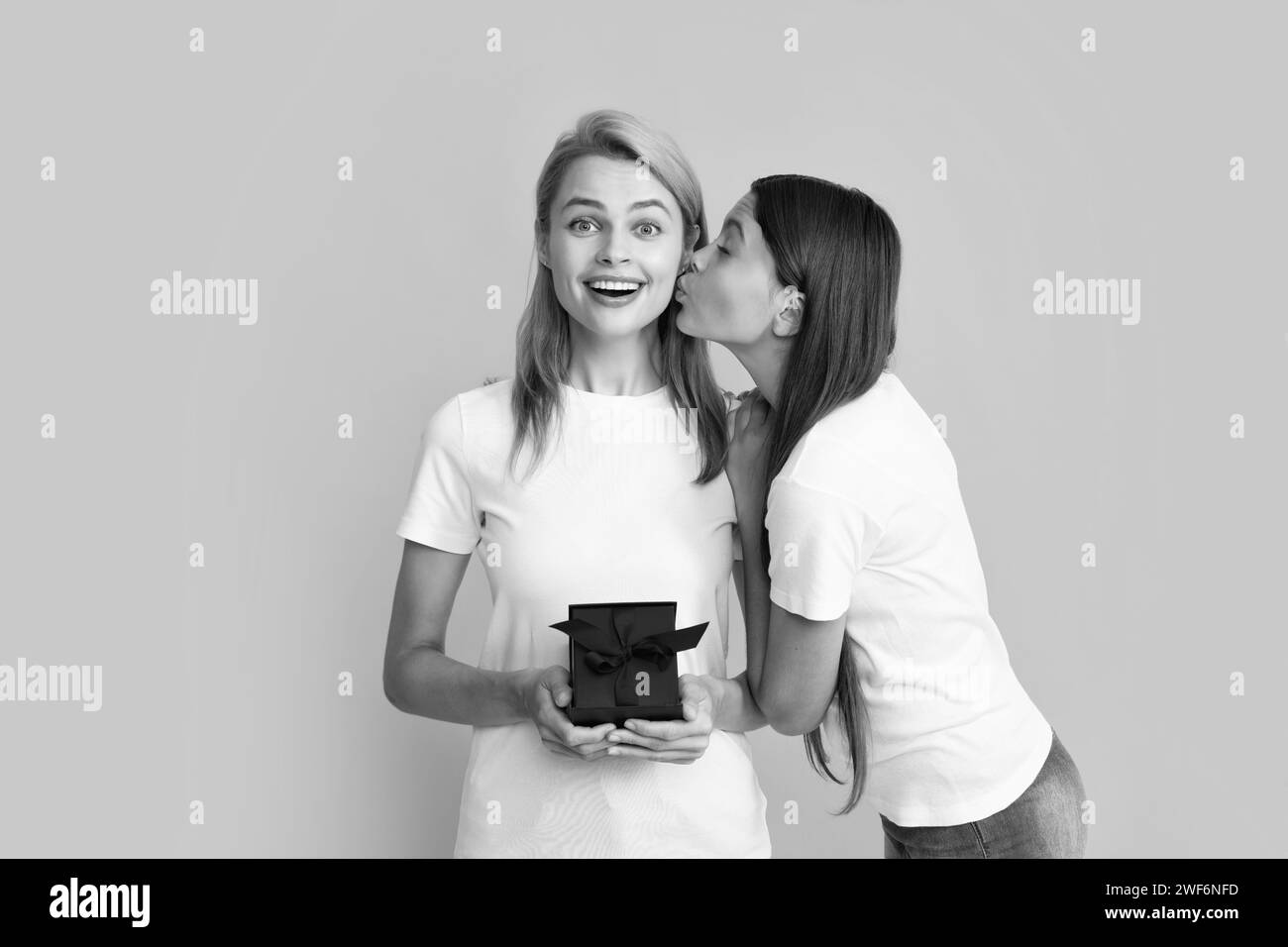 Kind küsst Mutter. Mutter und Tochter mit Geschenk. Teenager Mädchen gibt Geschenk-Box an ihre Mutter auf gelbem Hintergrund. Stockfoto