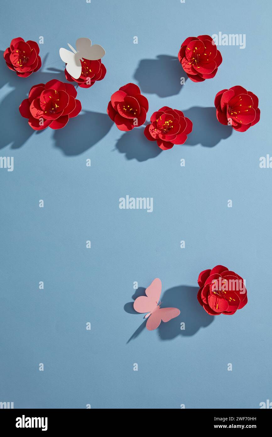 Ansicht von oben auf rote Papierblumen, weiße und rosa Schmetterlinge auf blauem Hintergrund. Leer für eine Werbekarte oder Einladung. Frühlingsblumen-Konzept. Flach Stockfoto