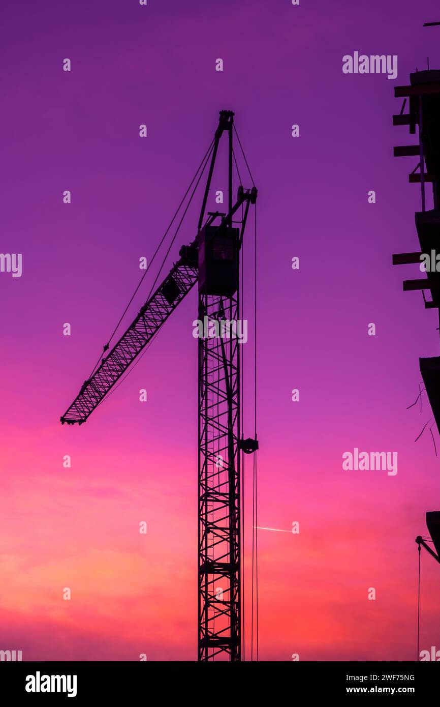 Silhouette von Baukranmaschinen in violettem Sonnenuntergang, vertikales Bild Stockfoto