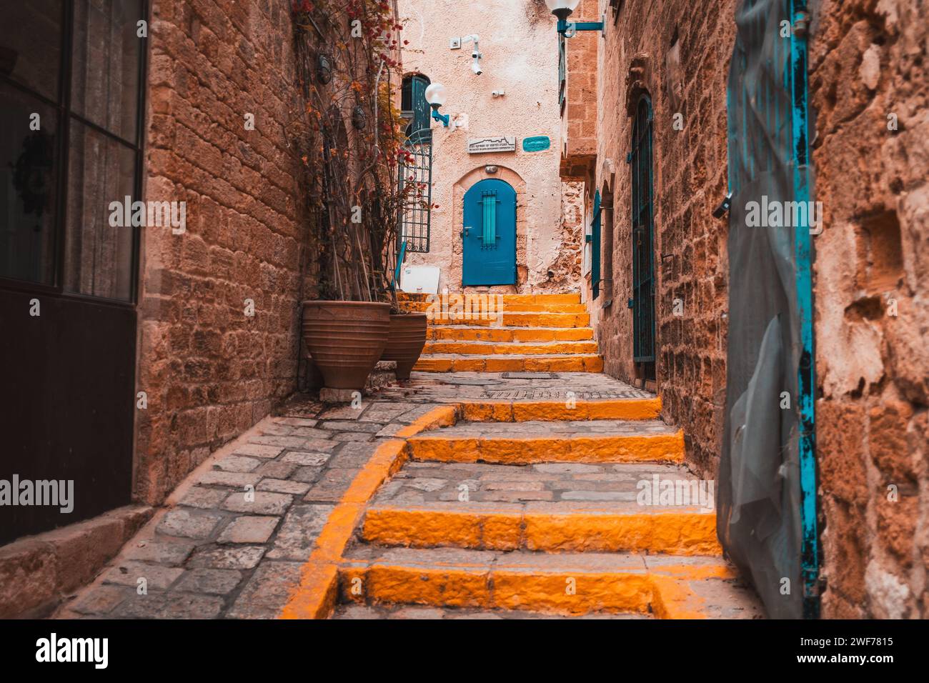 Der kopfsteingepflasterte Pfad und die lebendigen blauen Türen laden zu einem Spaziergang durch die historischen Gassen von Old Jaffa, Israel, ein. Stockfoto