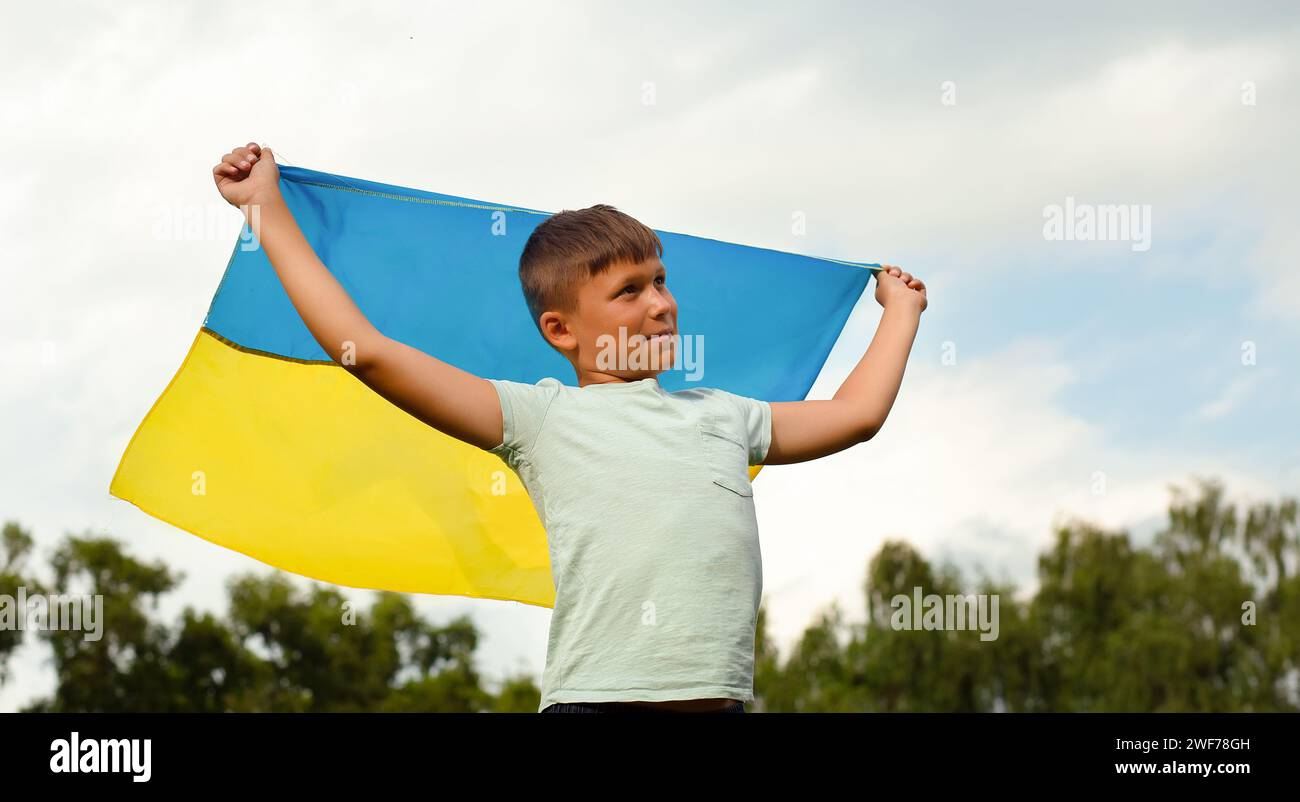 Glücklicher ukrainischer Junge, der mit wehender gelber und blauer Nationalflagge läuft, liebt das ukrainische Konzept. Unabhängigkeit, Flagge, Tag der Verfassung der Ukraine Stockfoto