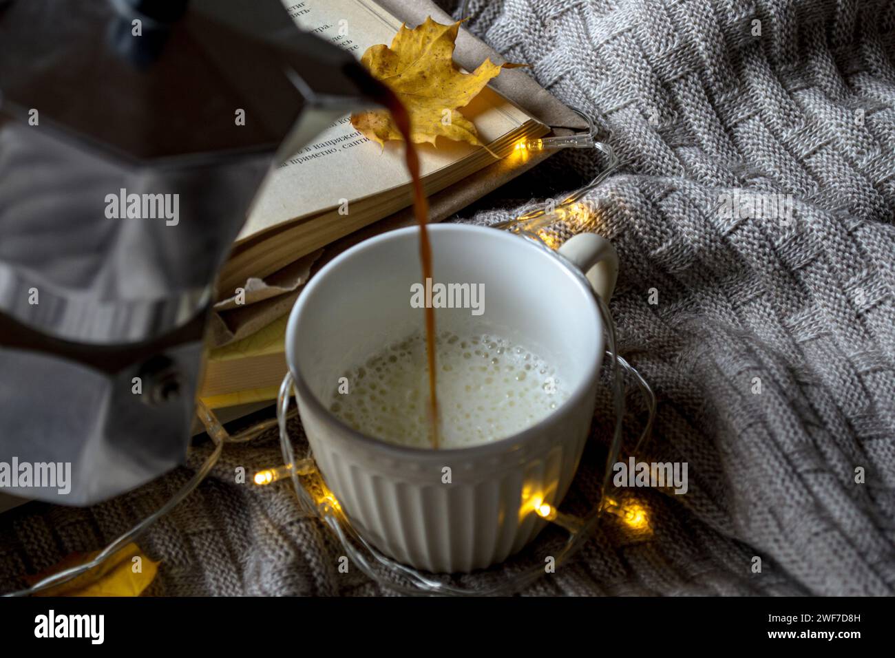 Eine Tasse heißer Kaffee, ein Stapel Bücher und gelbe Ahornblätter auf einem gestrickten Karo Stockfoto