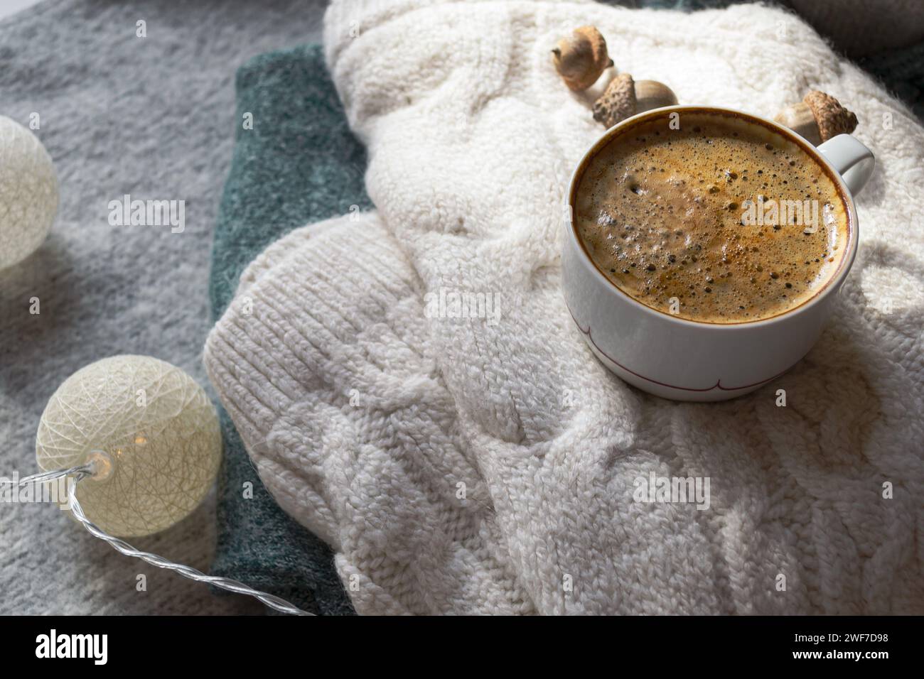 Warmer Strickpullover, heißer schwarzer Kaffee und ein Buch zum gemütlichen Lesen am Abend mit Girlanden Stockfoto