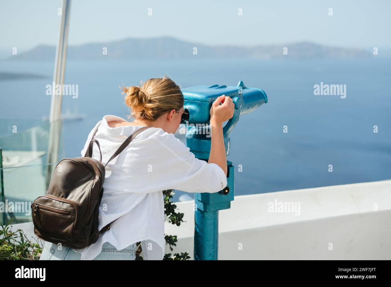 Die junge Frau schaut durch das Fernglas des Turms an der Küste von Santorin Stockfoto