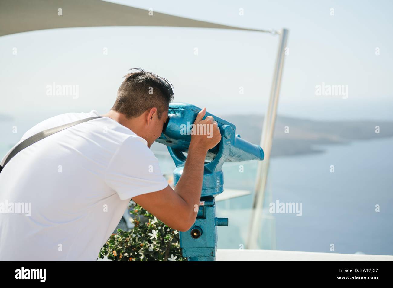 Mann, der durch das Fernglas des Turms auf die Küste von Santorin blickt Stockfoto