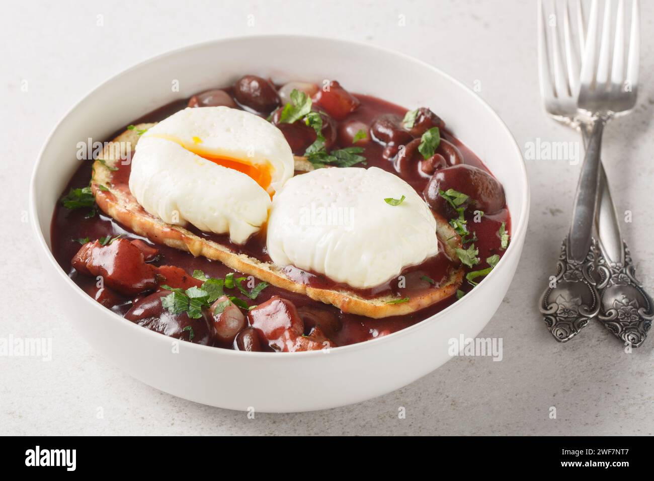 Oeufs en meurette Burgunderpochierte Eier mit Toast in Rotweinsauce mit Pilzen, Zwiebeln und Speck in Nahaufnahme auf einem Teller auf dem Tisch. Horizontal Stockfoto