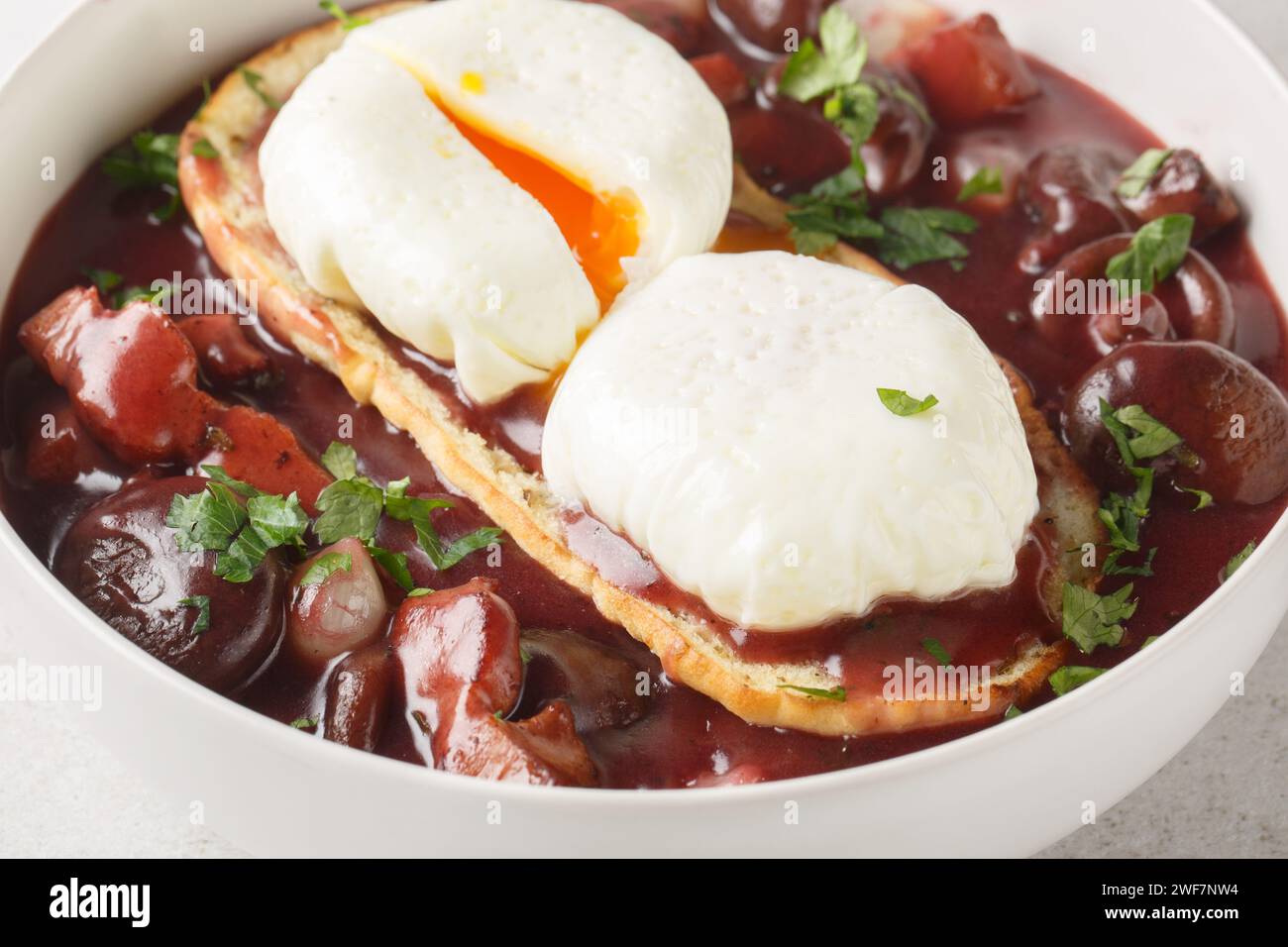 Pochierte Eier in Rotweinsauce mit Perlzwiebeln, Pilzen und Speck aus der Nähe auf dem Teller auf dem Tisch. Horizontal Stockfoto