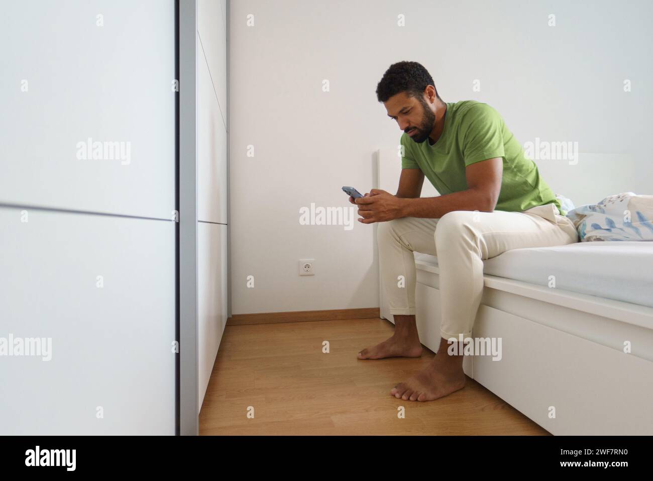 Ein Mann, der allein in seinem Bett aufwacht, auf das Smartphone schaut, SMS liest. Stockfoto