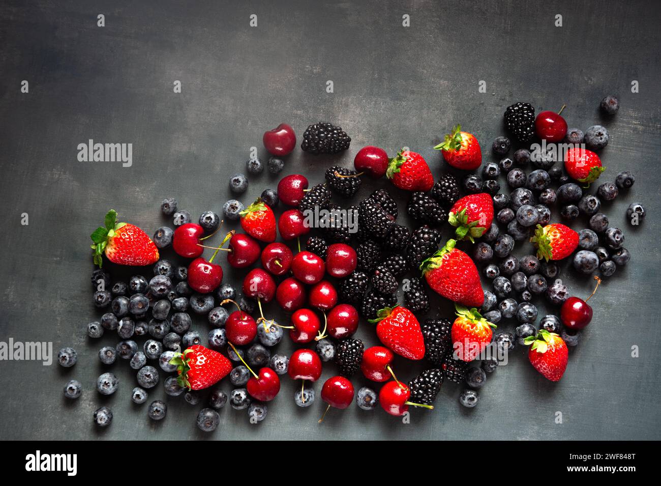Frische gemischte Beeren und Kirschen von oben auf einer grauen Oberfläche mit Kopierraum Stockfoto