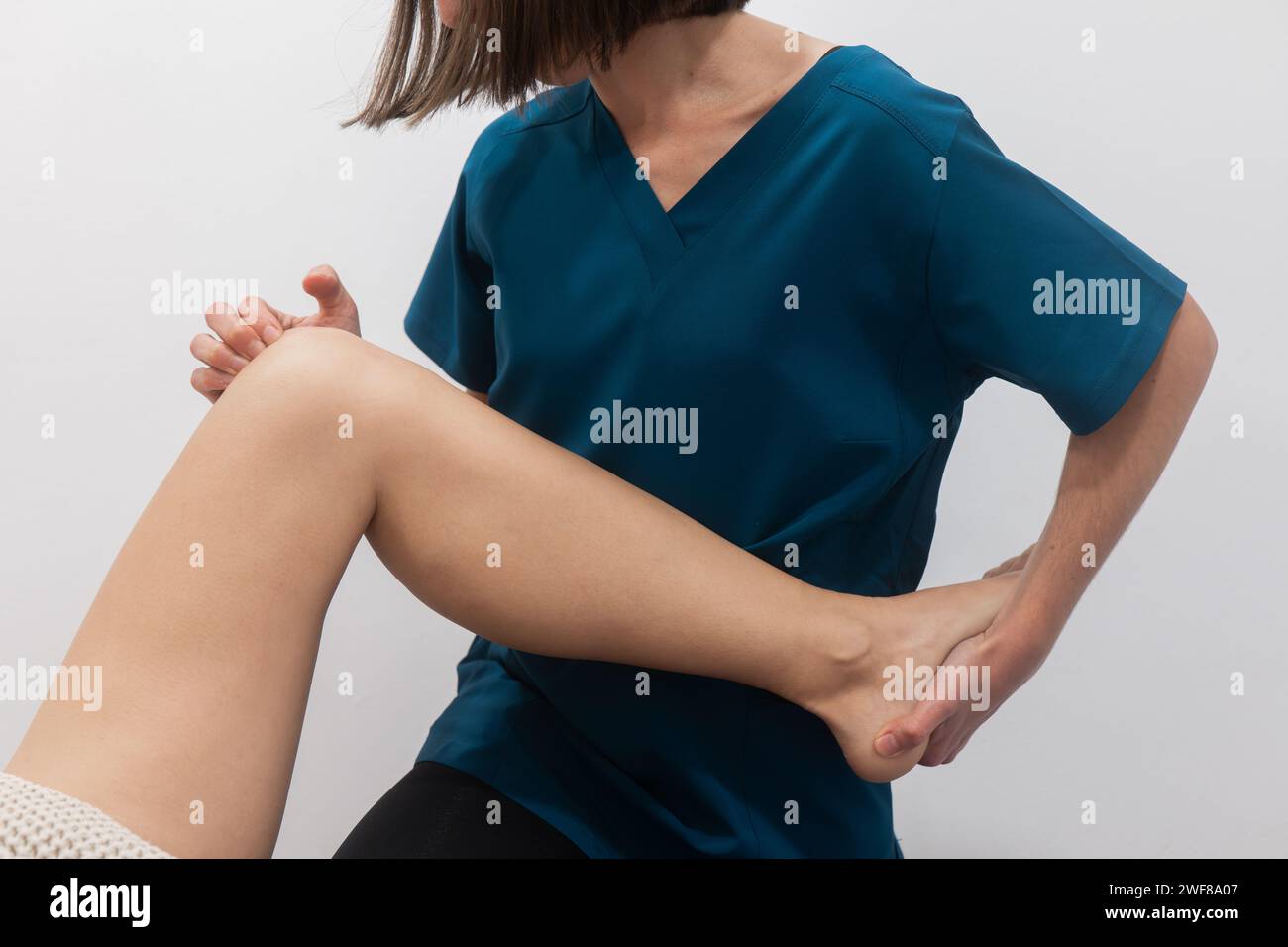 Ein Nahbild von jemandem in blauer medizinischer Kleidung, der seinen Knöchel hält, was auf Schmerzen oder Verletzungen hindeutet Stockfoto