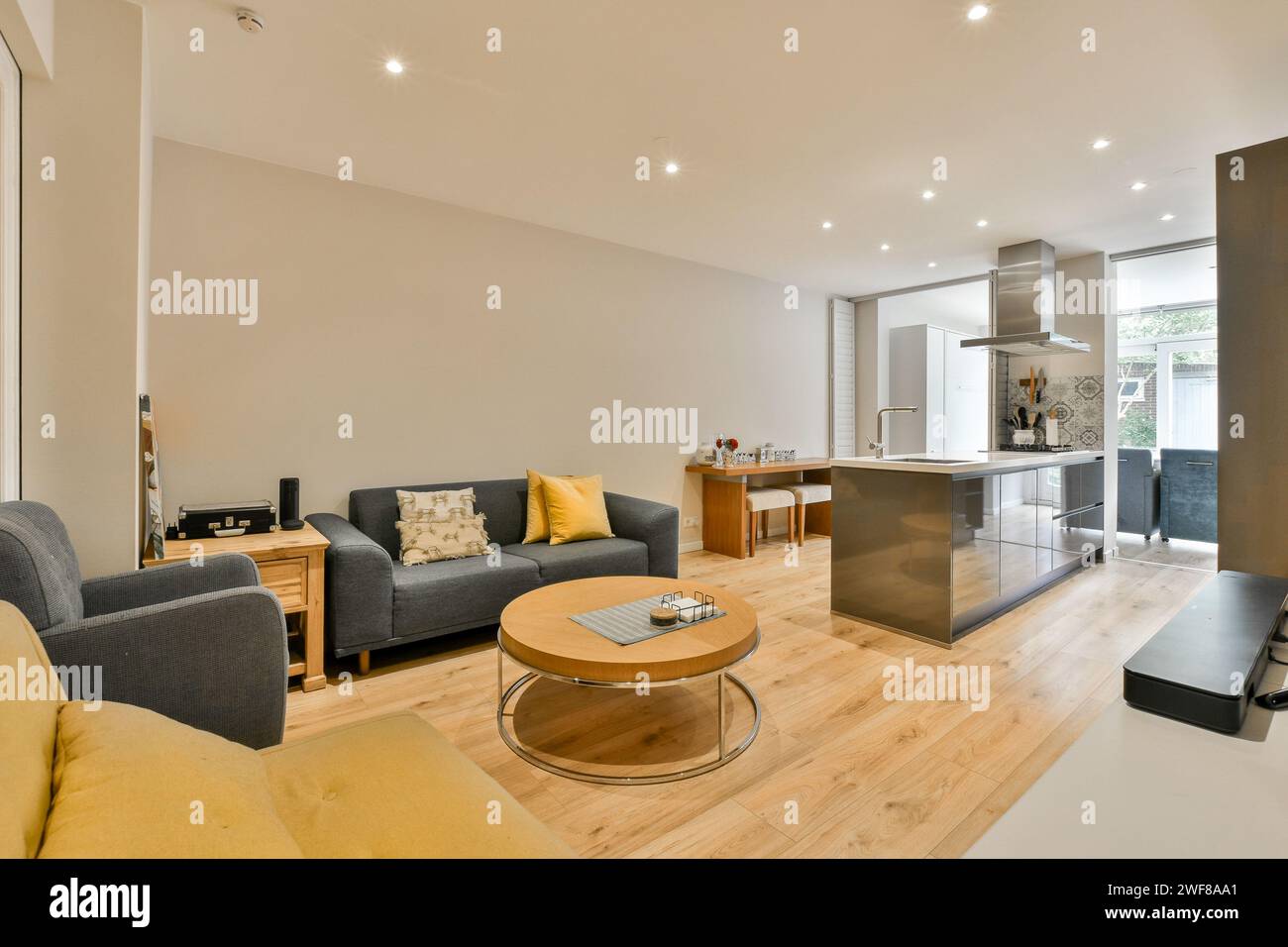 Ein geräumiges und modernes Wohnzimmer, das nahtlos in eine offene Küche übergeht, mit komfortablen Möbeln, Hartholzböden und hellem Licht Stockfoto