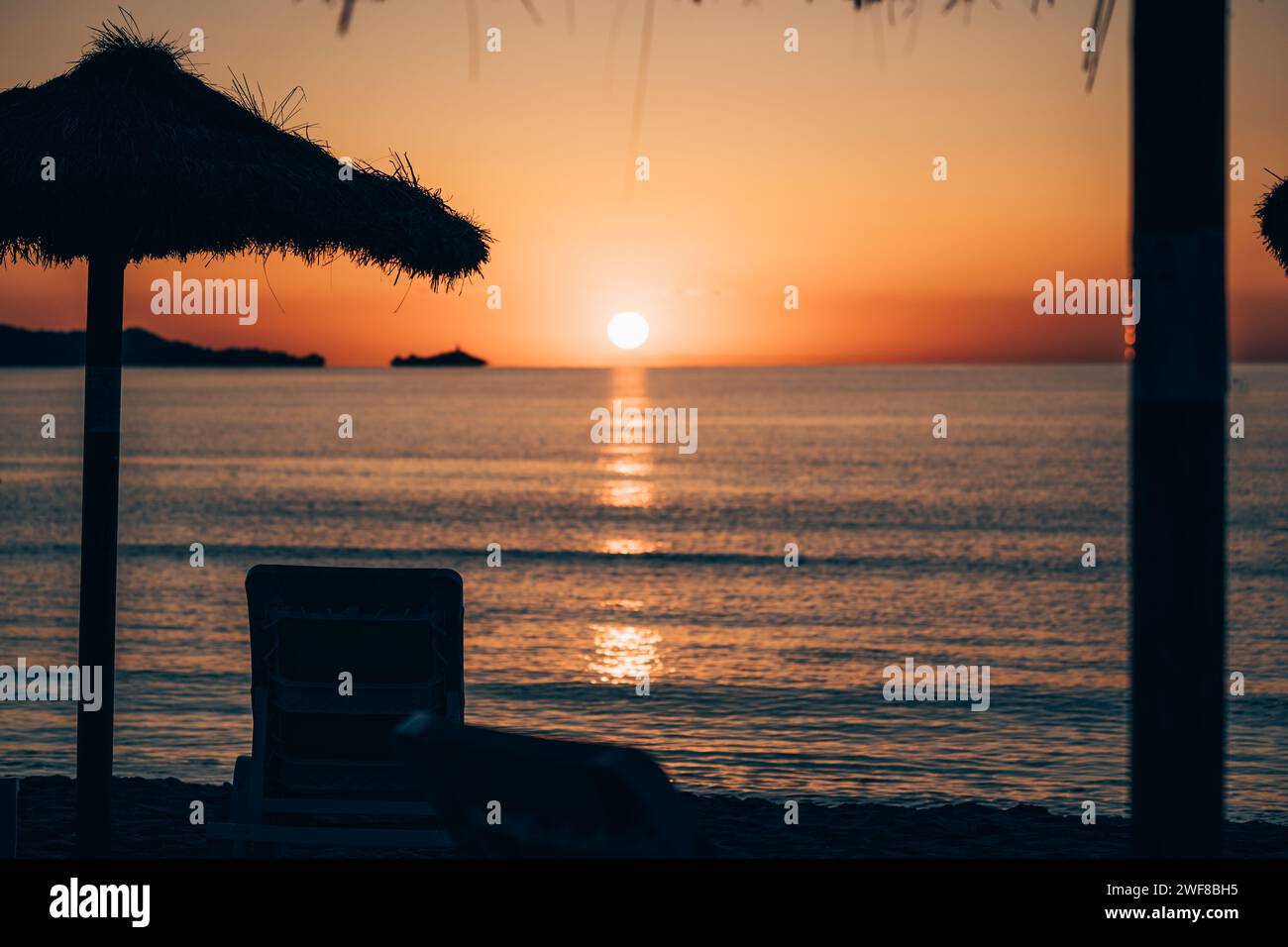 Ein Sonnenuntergang über dem Meer mit Liegestühlen am Ufer an einem schönen Tag Stockfoto