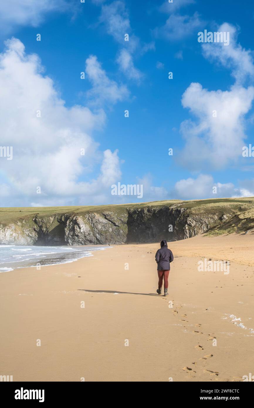 Eine Frau, die allein am goldenen Sand am Holywell Beach in Newquay in Cornwall in Großbritannien spaziert. Stockfoto
