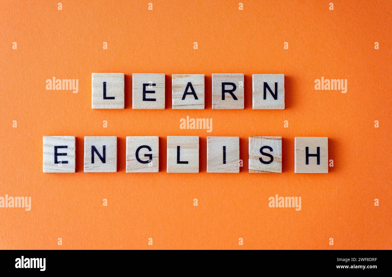 Word Englisch lernen. Motivation. Der Satz ist in Holzbuchstaben von oben angeordnet. Motivation. Orangefarbener flacher Lay-Hintergrund Stockfoto