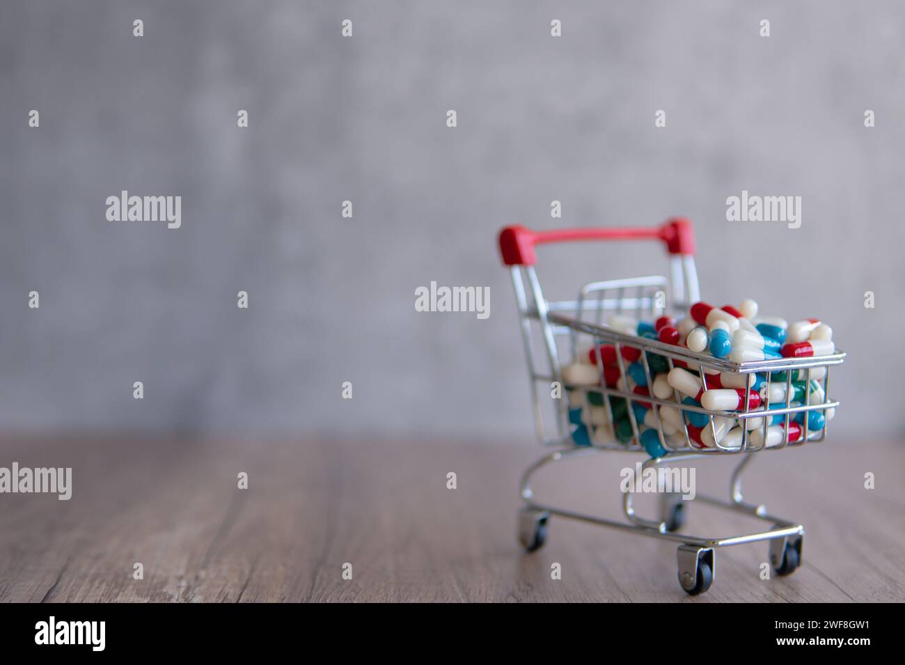 Ein Einkaufswagen voller bunter Pillen auf einem Holztisch. Kopierbereich für Text. Online-Apotheke, Gesundheitskosten Konzept. Stockfoto