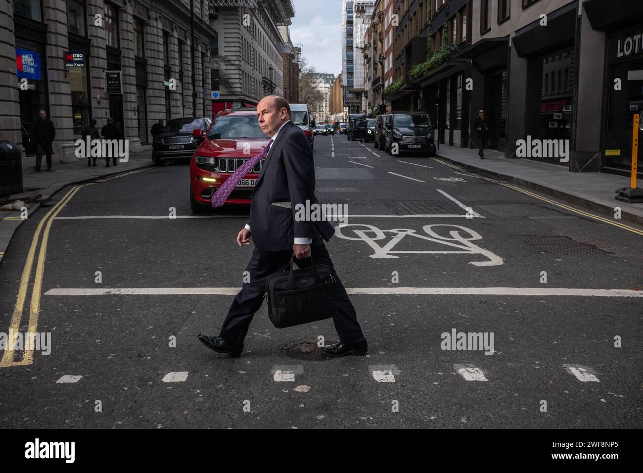 Ein Geschäftsmann spaziert entlang Piccadilly in Mayfair, während der Wind an einem stürmischen Winternachmittag in London, England, Großbritannien, seine violette Anzug-Krawatte weht Stockfoto