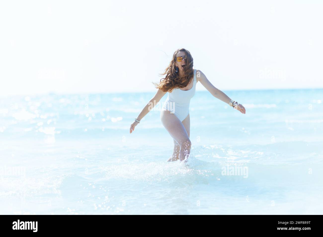 Lächelnde, moderne Frau am Strand, die Spaß im Wasser hat. Stockfoto
