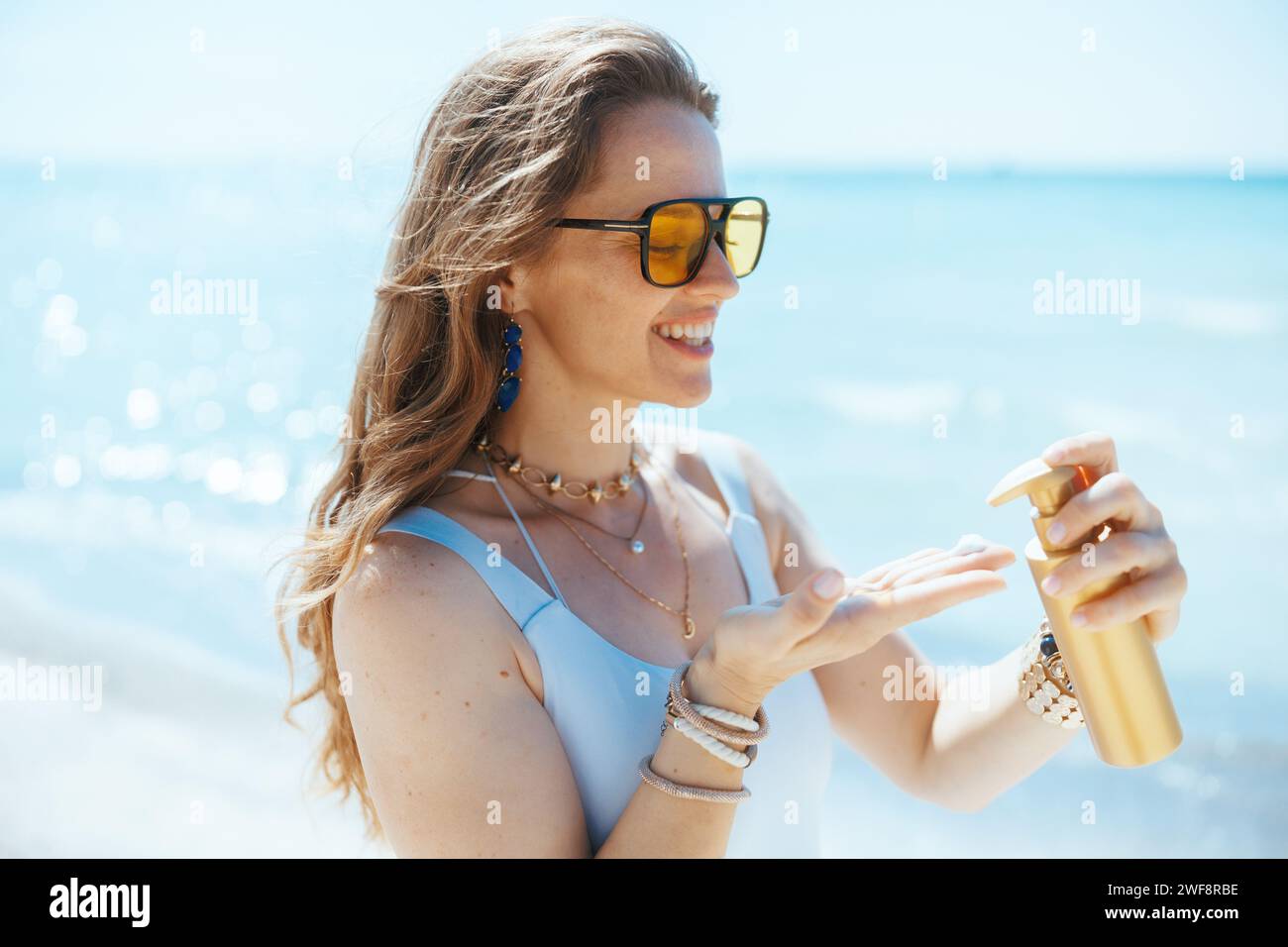Lächelnde elegante Frau mittleren Alters an der Küste mit Sonnencreme. Stockfoto