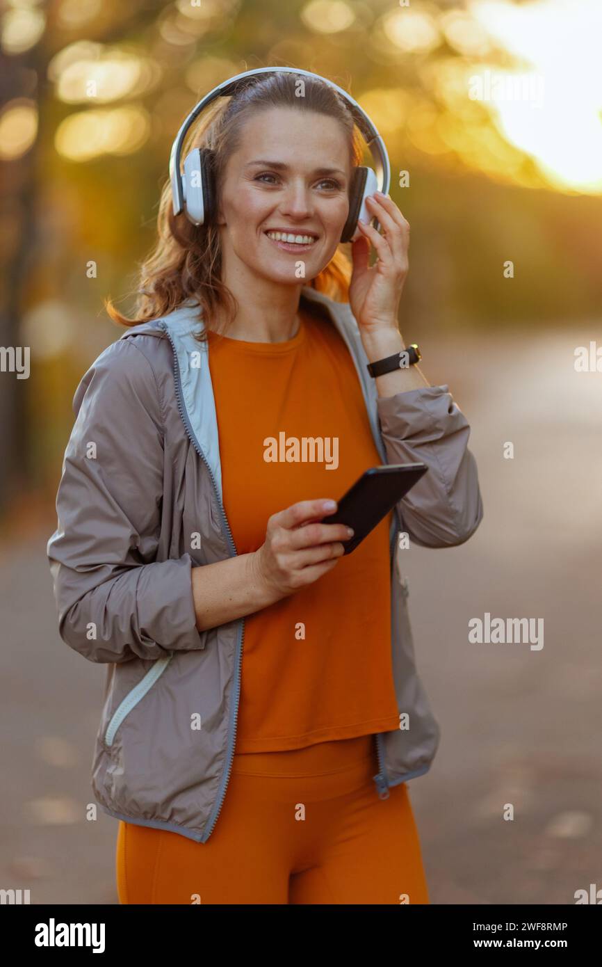 Hallo Herbst. Frau mit glücklicher Passform in Fitnesskleidung im Park mit Kopfhörern. Stockfoto