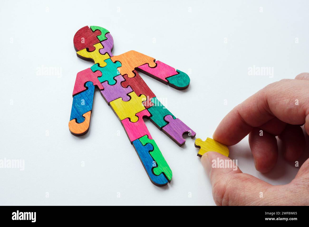 Eine Hand stellt eine Figur aus mehrfarbigen Puzzles als Konzept des Autismus zusammen. Stockfoto