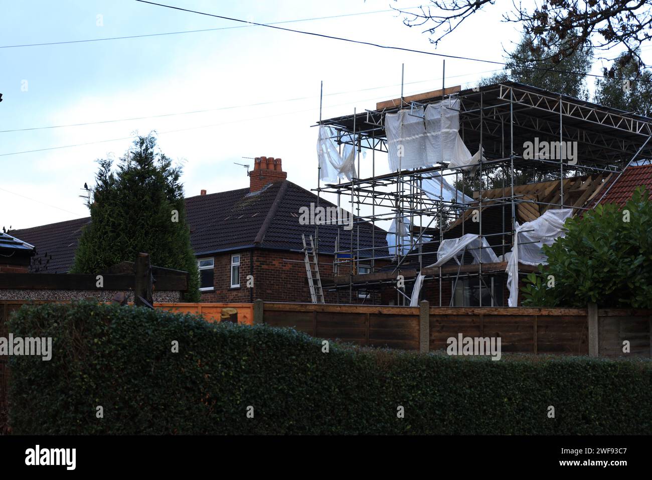 Ein Sturmschaden: Großes Haus mit Gerüsten auf dem Dach, umgeben von Holz- und Ziegelbauten Stockfoto