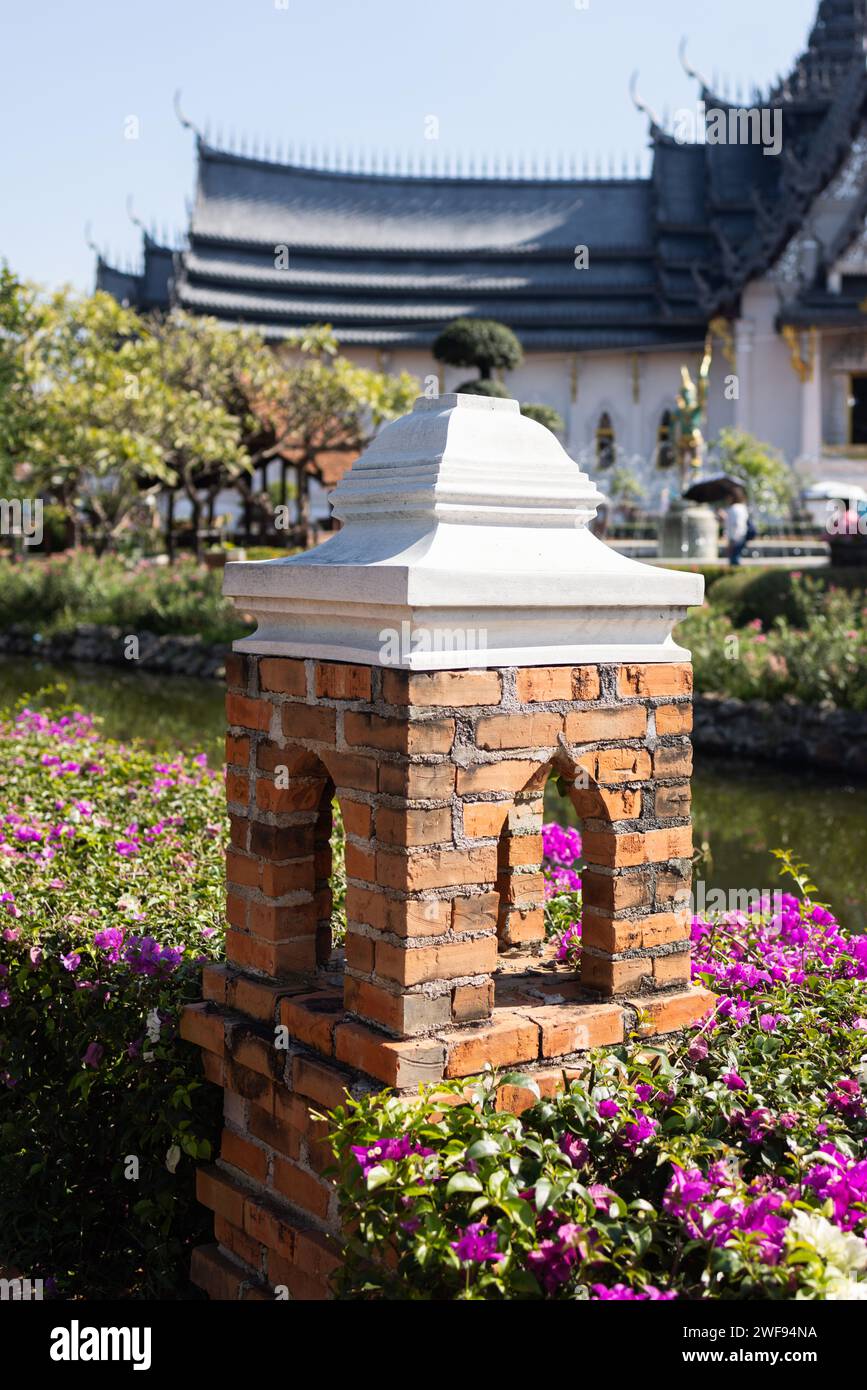 Ein Backsteinturm mit einer weißen Spitze steht hoch in einem wunderschönen Garten umgeben von üppigem Grün. Stockfoto