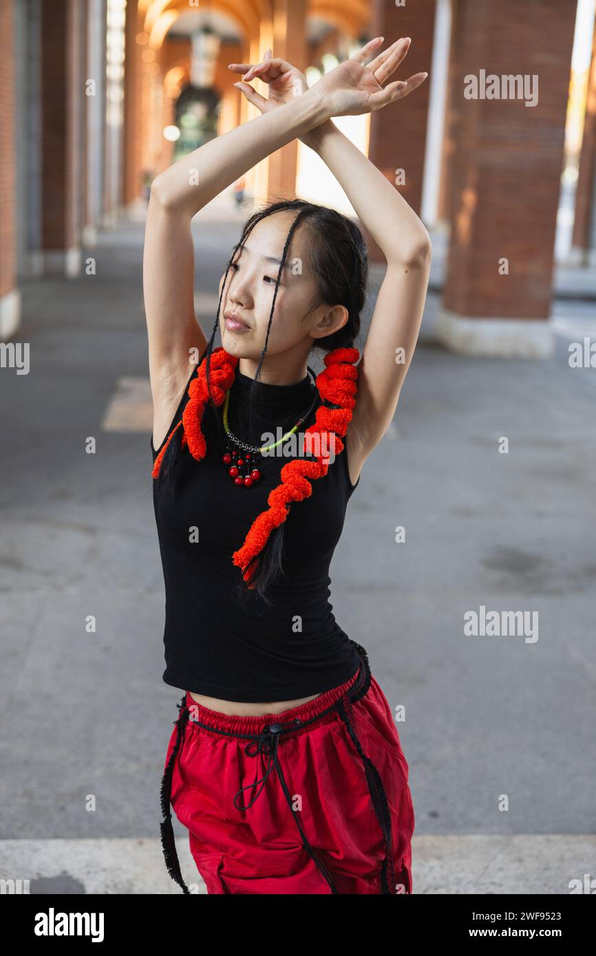 Eine Stadttänzerin in dynamischer Bewegung, ihre Arme anmutig über dem Kopf positioniert und mit einem leuchtend roten Schal verziert. Stockfoto