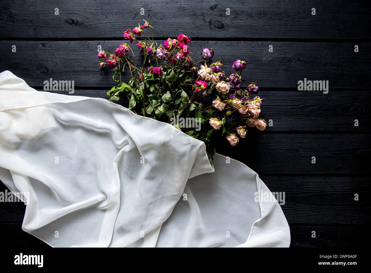 Ein Strauß getrockneter Rosen und ein weißer Schal liegen auf einem schwarzen Holzbrett, ein Strauß getrockneter Blumen auf dem Tisch Stockfoto