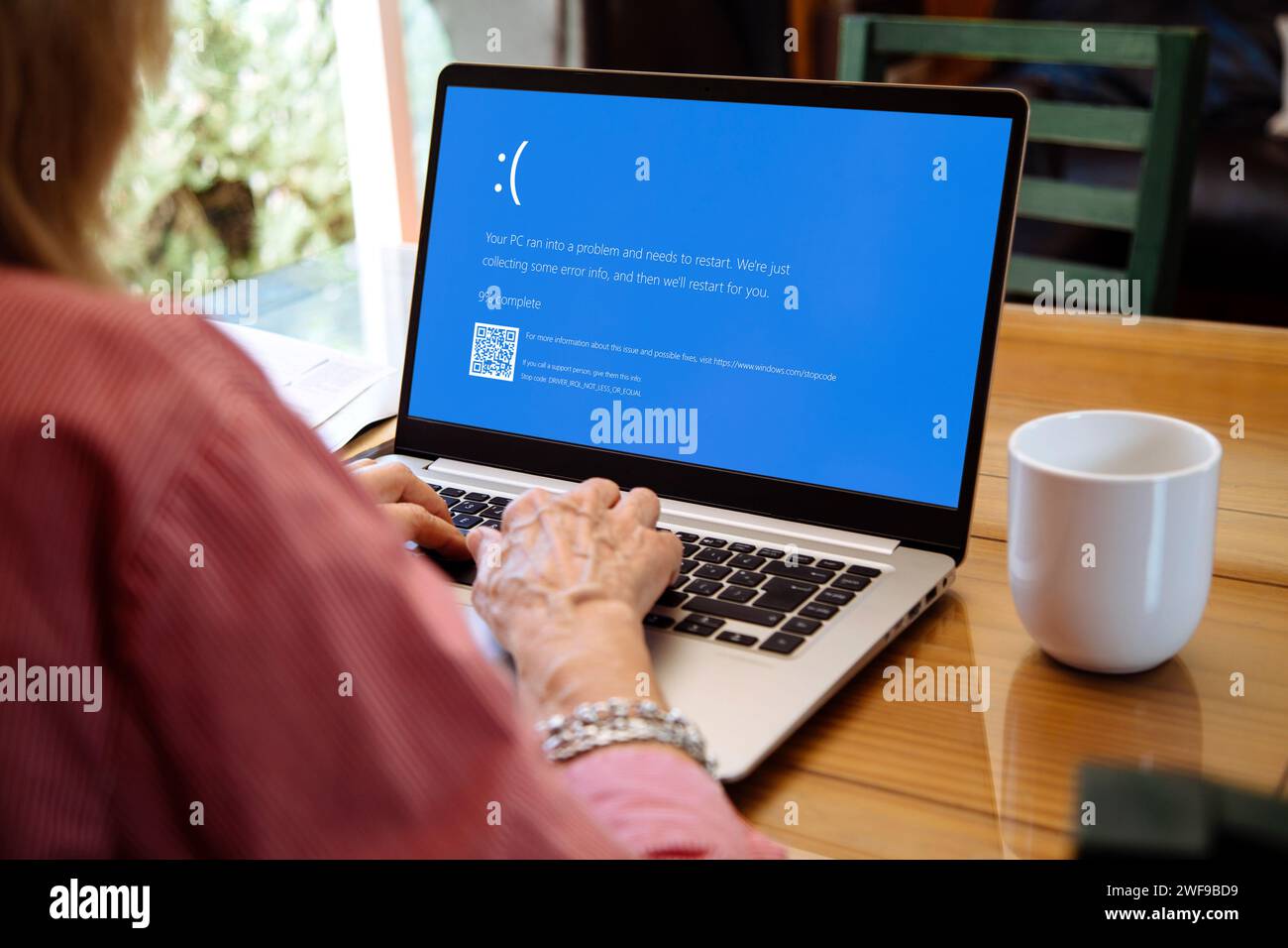 Frau mit Laptop, die auf dem Monitor den blauen Bildschirm des Todes oder BSOD anzeigt. Fehlerhaftes Microsoft-Betriebssystem Windows 10. Stockfoto