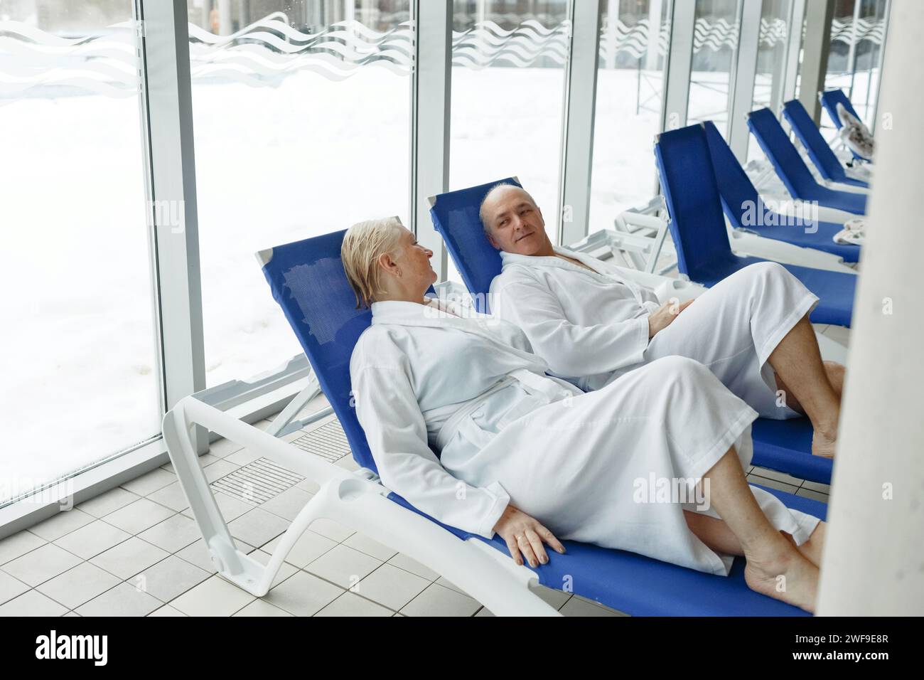 Eine ältere Frau mit einem Mann in Bademänteln auf einer Liege am Pool. Entspannen Sie sich im Spa-Center. Stockfoto