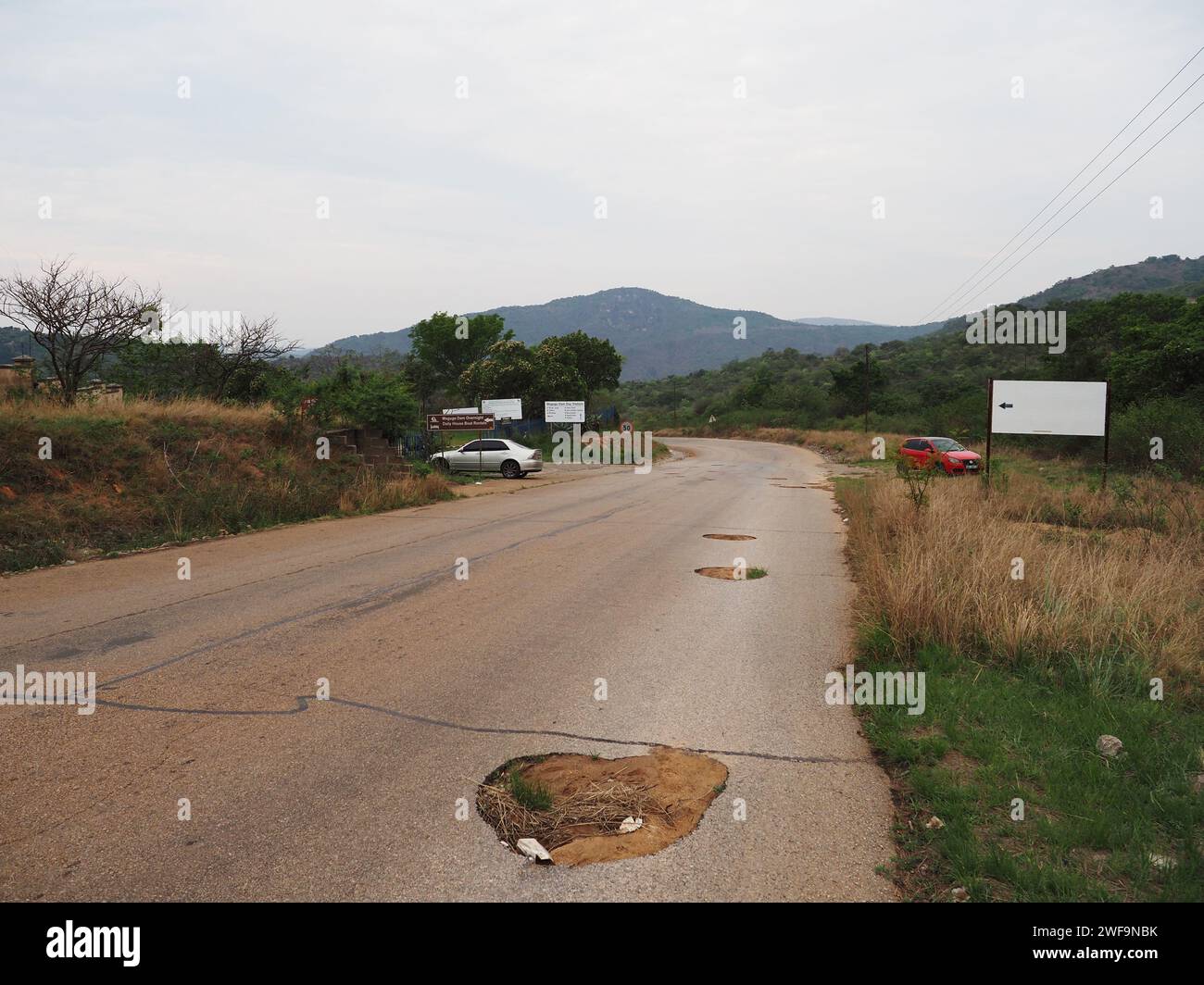 Viele große Schlaglöcher und sehr schlechte Straßenoberfläche der Maguga-Damm-Straße in Piggs Peak, Eswatini. Stockfoto