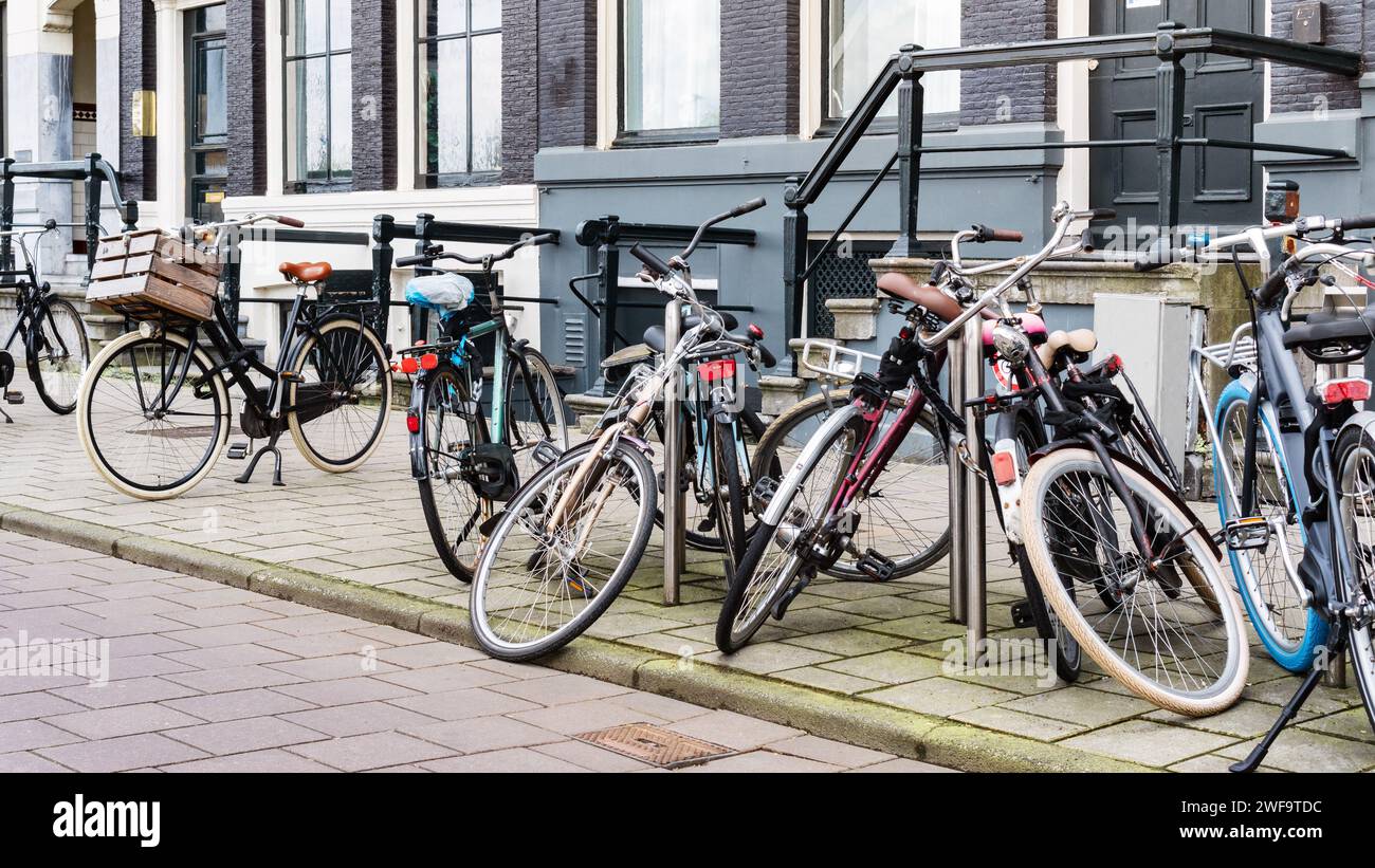 Alte Freizeitfahrräder parkten achtlos entlang einer Straße in der Nähe eines Stadthauses in Amsterdam. Ein Fahrradparkplatz an einer Stadtstraße. Öffentliche Fahrradtour Stockfoto