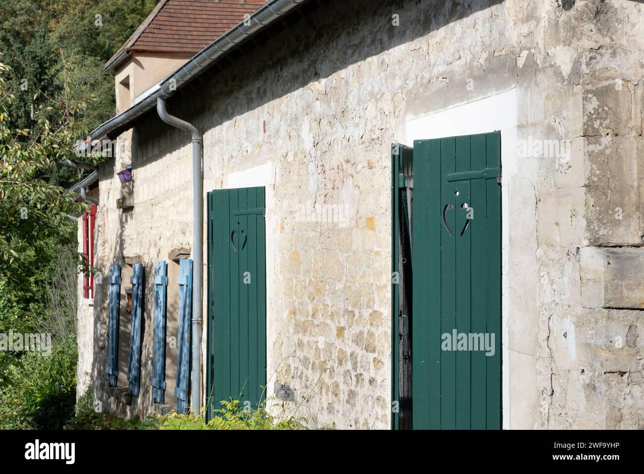 Haus in Auvers-sur Oise in Frankreich mit verwitterten verputzten Wänden und Fenstern mit unterschiedlich farbigen Fensterläden, rot, blau und grün Stockfoto