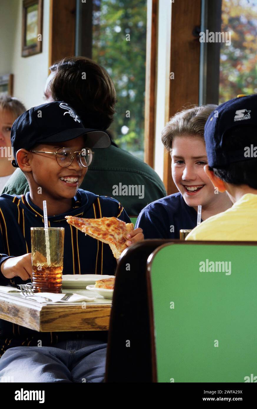 Eine Gruppe junger Teenager, die an einem Restauranttisch sitzen, Pizza essen und Gespräche führen. Stockfoto