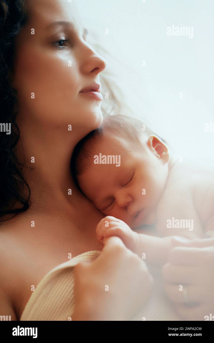 Eine Frau, die sanft ein neugeborenes Baby in ihren Armen einlegt und einen zarten Moment der Liebe und Pflege schafft. Stockfoto