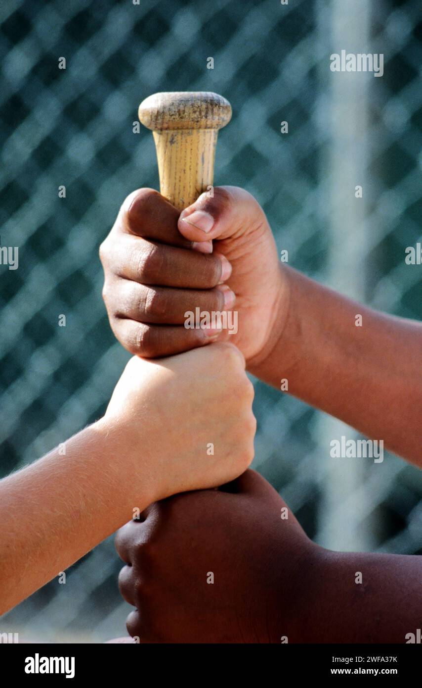 Afroamerikanische und kaukasische Hände greifen einen Baseballschläger in der altehrwürdigen Methode der Wahl Stockfoto