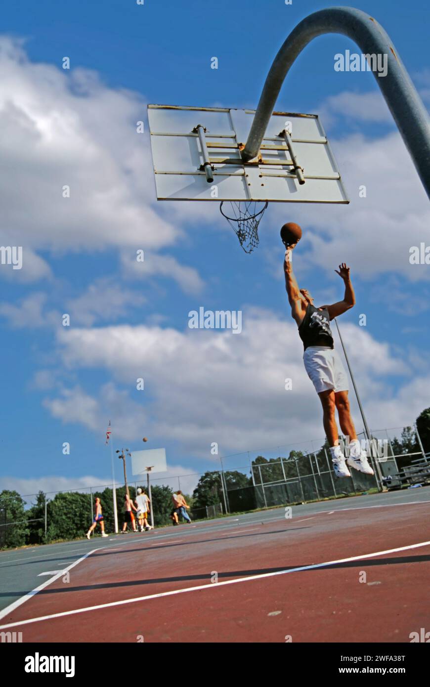Ein Mann, der Basketballkleidung trägt, springt hoch, während er den Basketball hält, um ihn in den Korb zu tauchen. Stockfoto