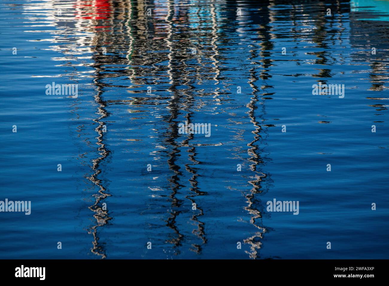 Das ruhige blaue Wasser erzeugt ein faszinierendes abstraktes Muster, das die verzerrte Silhouette und Lichter von Booten in der Abenddämmerung reflektiert. Stockfoto