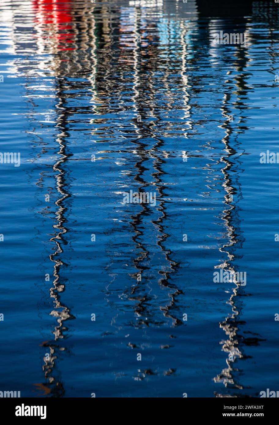 Das ruhige blaue Wasser erzeugt ein faszinierendes abstraktes Muster, das die verzerrte Silhouette und Lichter von Booten in der Abenddämmerung reflektiert. Stockfoto