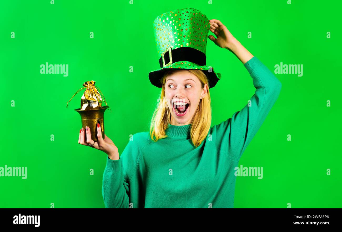 Feierlichkeiten zum St. Patrick-Tag. Blonde Frau in grünem Pullover und Leprechaun-Hut. Patricks-Tag. Glückliches Mädchen in grünem Hut mit einer kleinen Tasche Gold. Topf mit Stockfoto