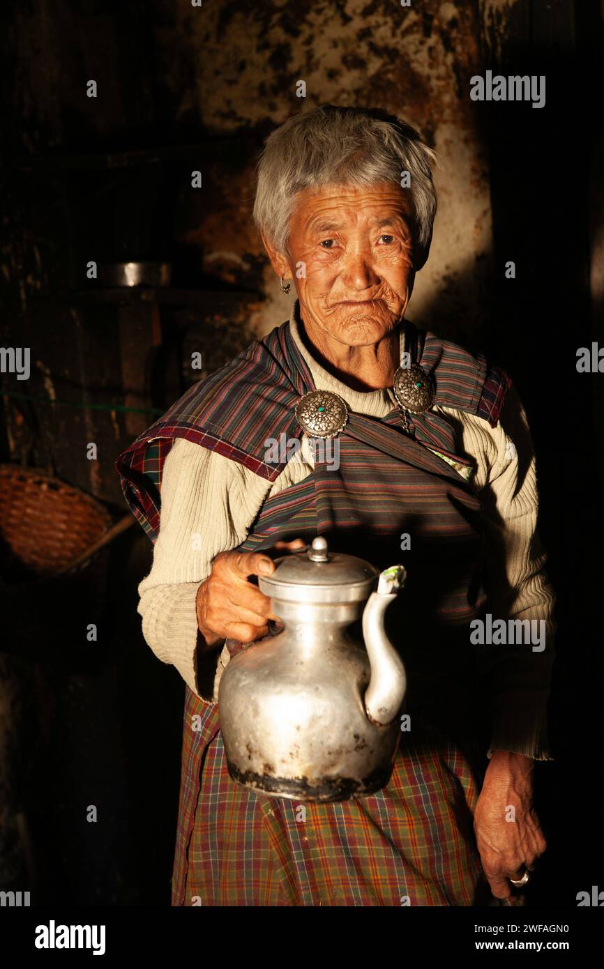 Eine ältere Bhutaneserin in ihrer rustikalen Küche bietet frisch zubereiteten, heißen Yak Butter Tee aus einer Metall-Teekanne im Dorf Ogyen Choling, Bumthang Valle Stockfoto