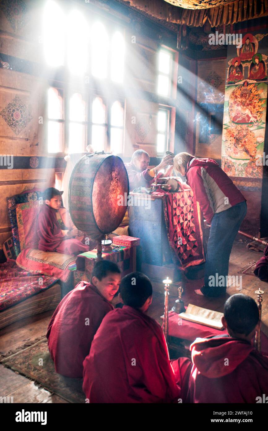 Lama schenkt einem Touristen einen Segen für eine sichere Heimreise während einer Zeremonie bei Sonnenaufgang, wenn Sonnenstrahlen durch die staubigen Fensterscheiben strömen Stockfoto