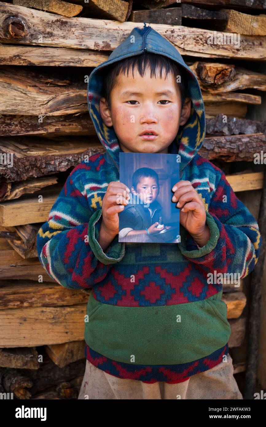 Der junge bhutanische Junge hält ein Foto von ihm, das vor einem Jahr vor seinem Haus, Ugyen Choling Village, Bhutan, Asien, aufgenommen wurde Stockfoto