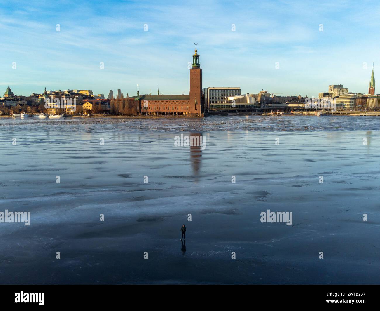 Das Rathaus von Stockholm im Winter, mit Eis auf dem See Malaren. Ein Mann, der auf dem Eis im Vordergrund steht. Helles Licht, blauer Himmel. Winter. Stockfoto