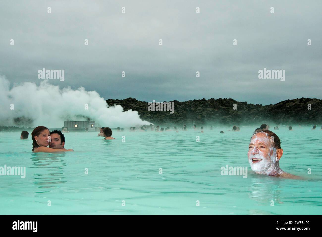 Touristen, die in der Blauen Lagune, Island, das warme Mineralwasser mit Kieselsäure auf ihren Gesichtern genießen Stockfoto