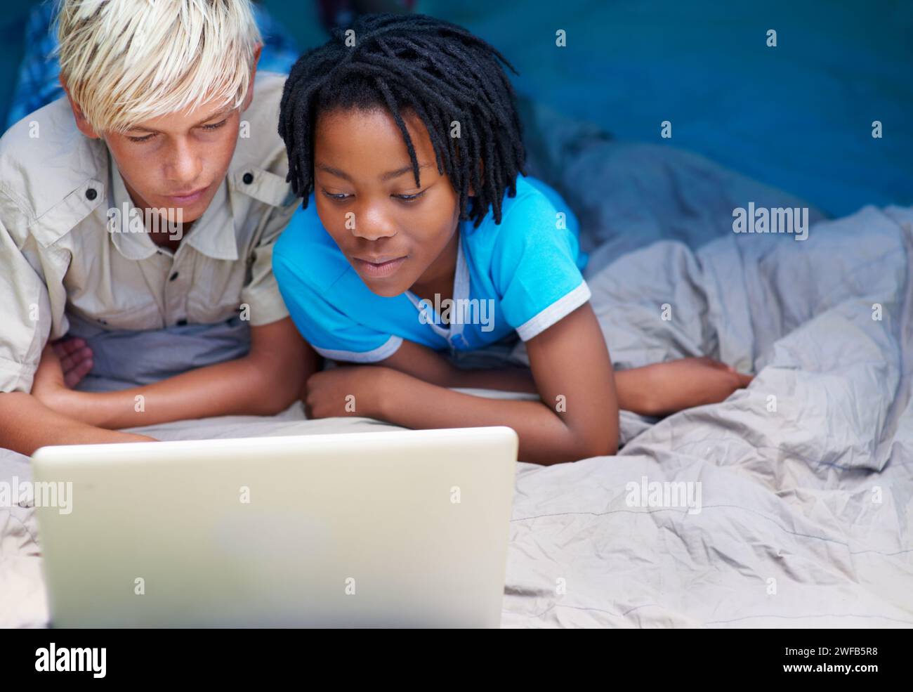 Kinder können sich entspannen und im Urlaub einen Laptop im Bett zusammen mit Zeichentrickfilm, Film oder Online-Spielen ansehen. Kinder, lächeln und spielen mit dem Computer Stockfoto